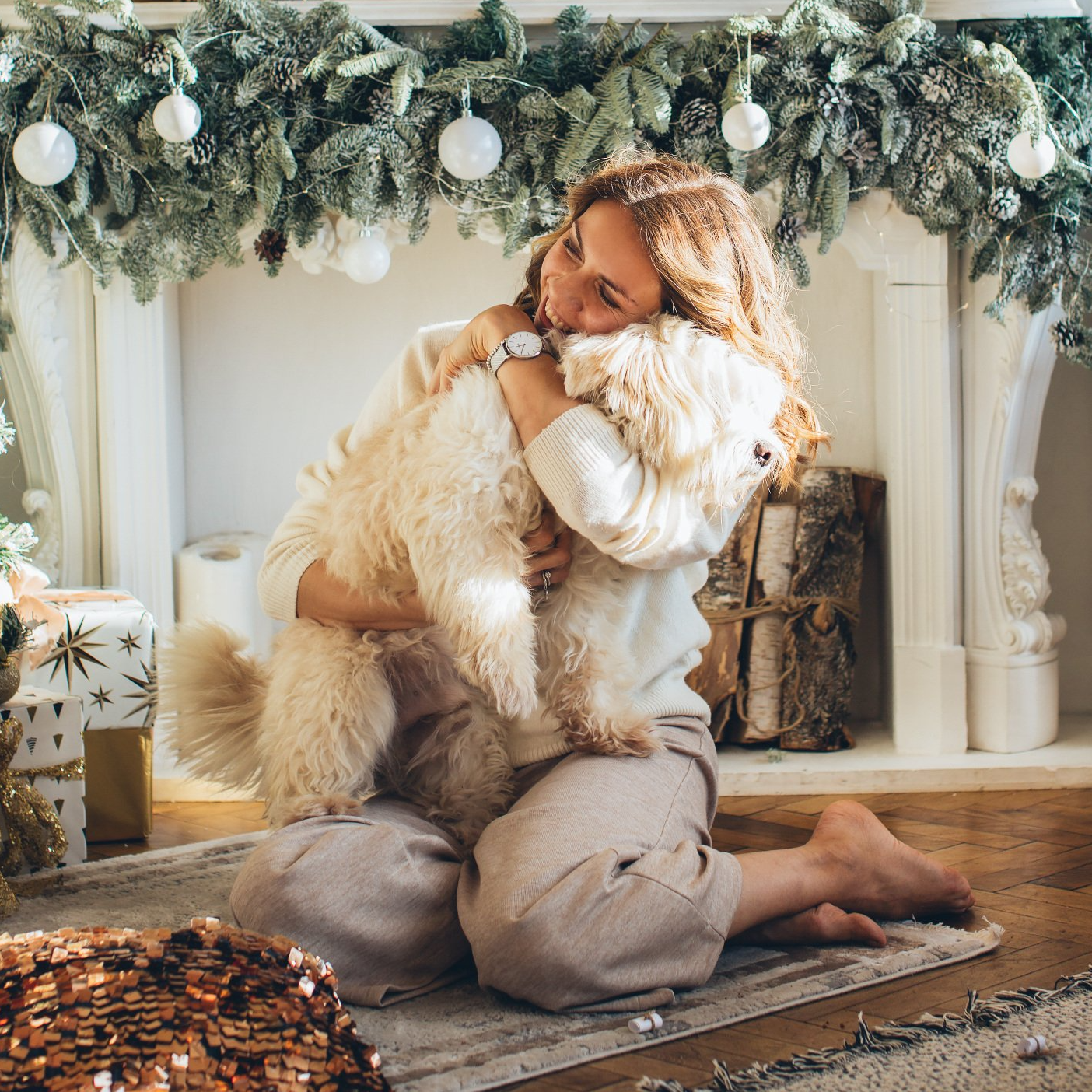 a woman is kneeling on the floor holding a dog in front of a fireplace .