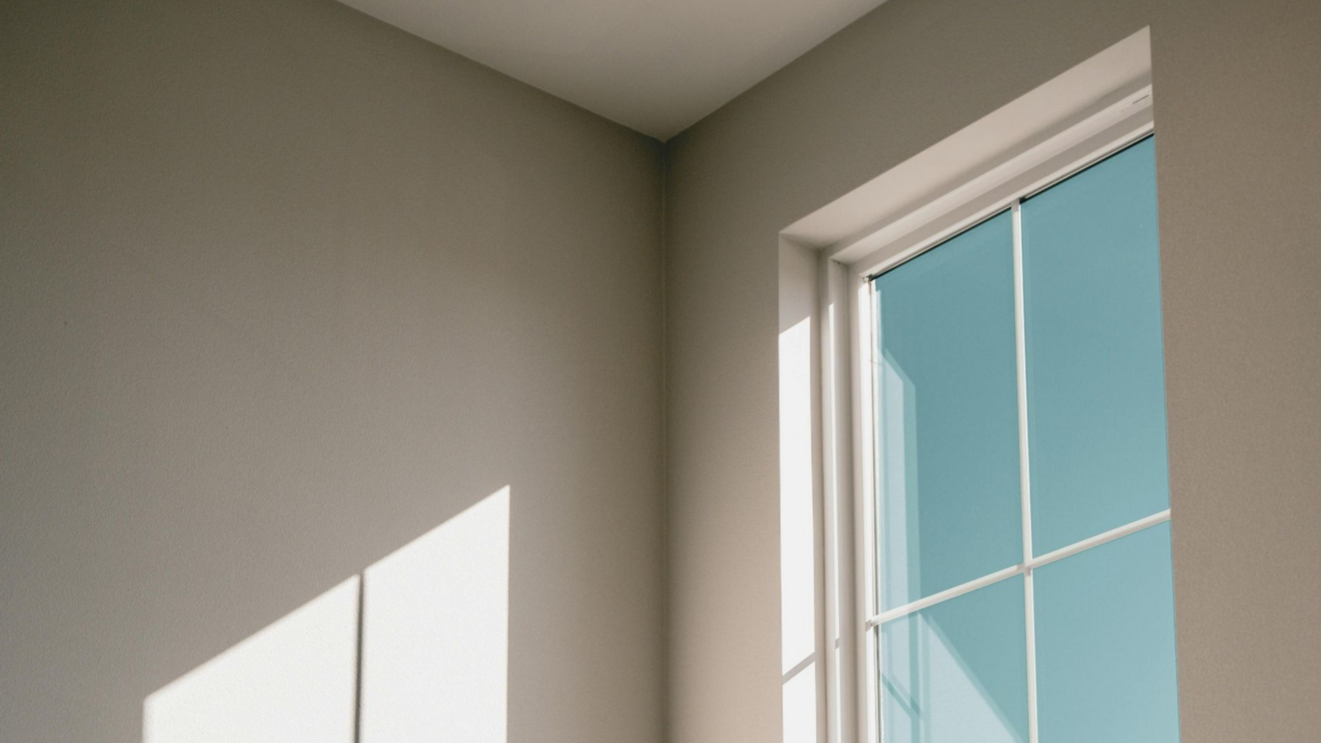 Corner of a room with a window; white trim, sunlight on walls, muted blue sky visible.