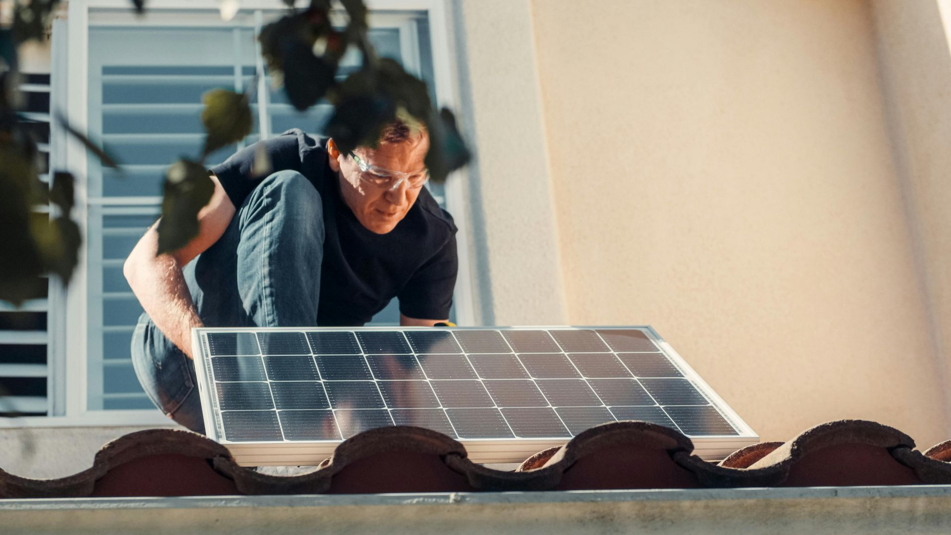 Man installing a solar panel on a rooftop, wearing safety glasses.