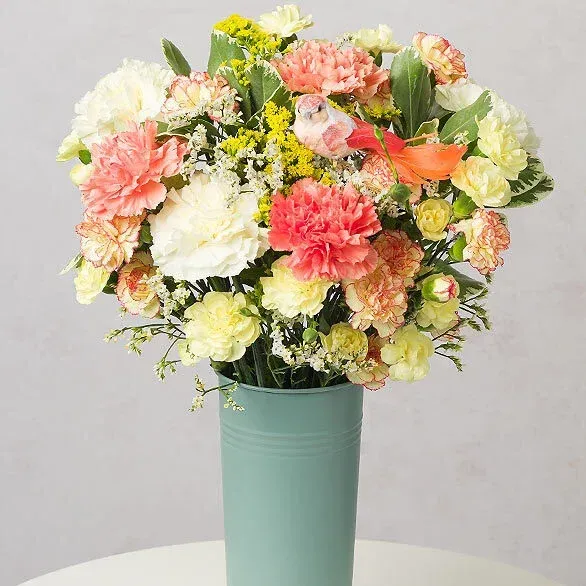A vase filled with flowers and a bird on a table.