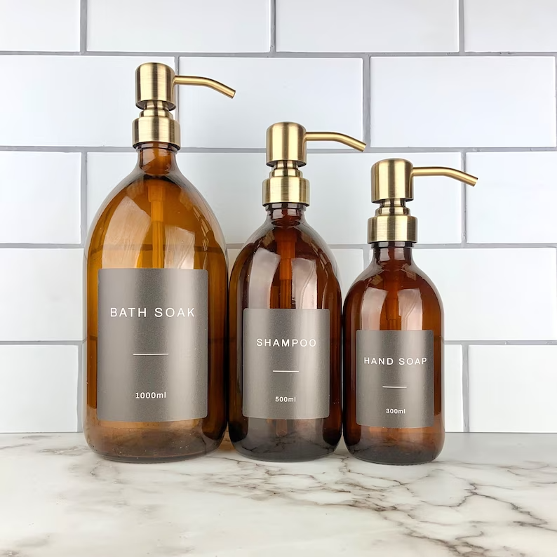 Three bottles of bath soap , shampoo , and hand soap are sitting on a marble counter.