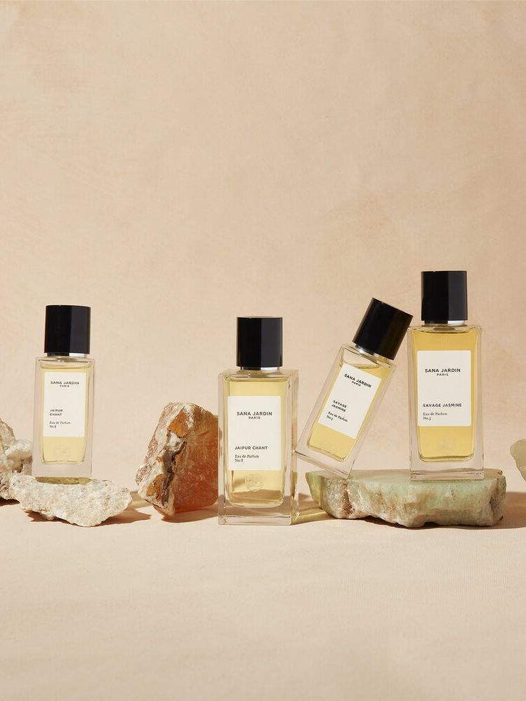 four bottles of perfume from Sana Jardin are sitting on top of rocks on a table .
