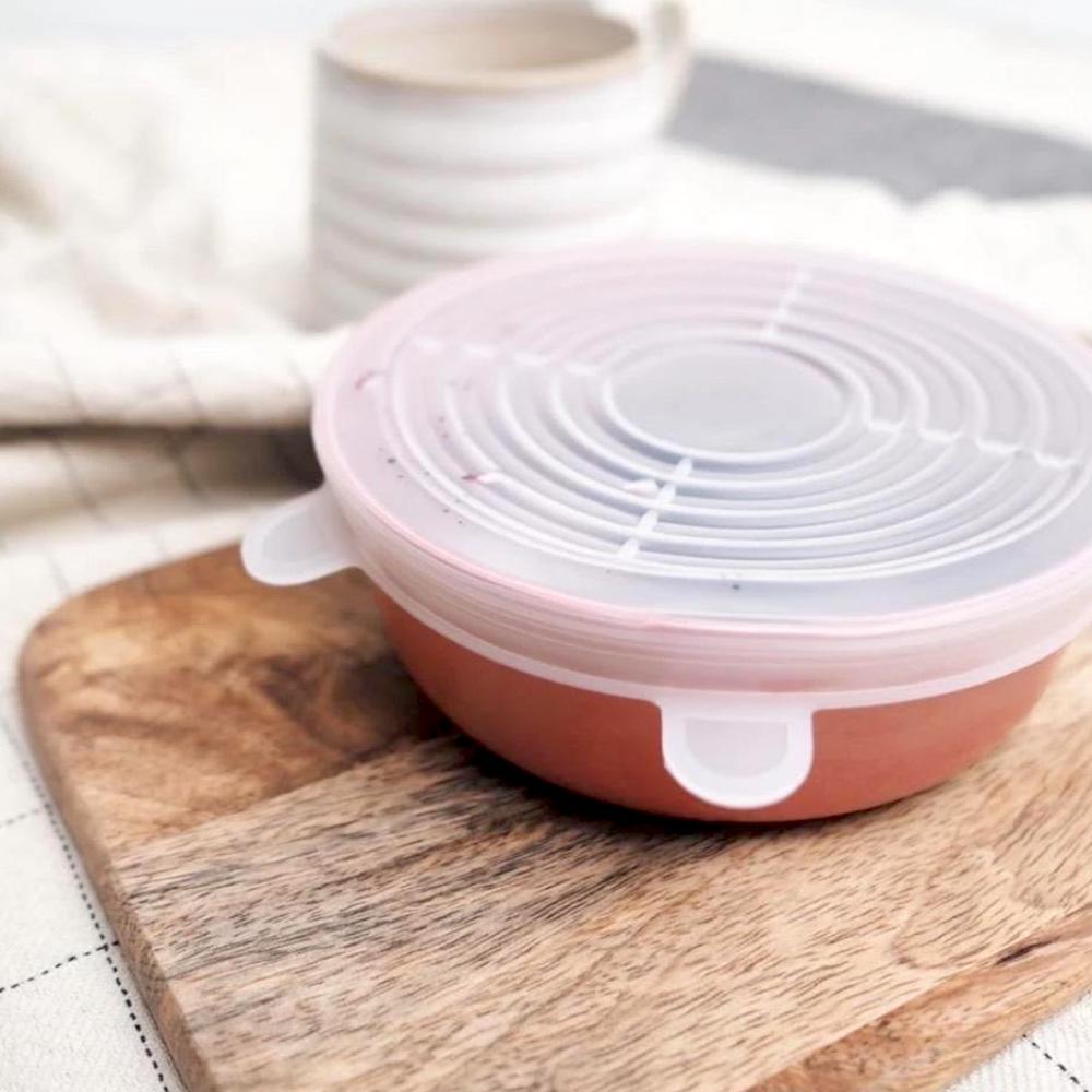 A bowl with a pink lid is sitting on a wooden cutting board.