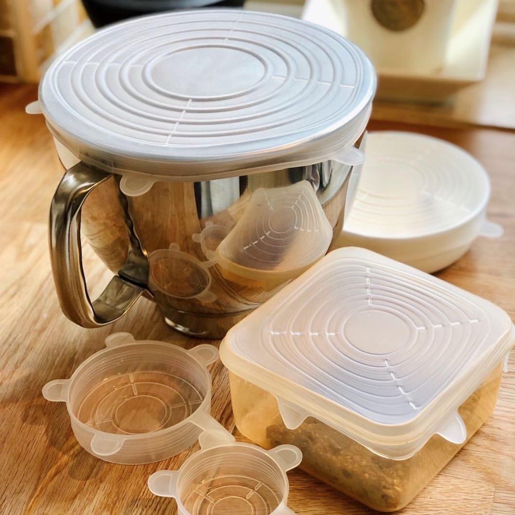 A blender with a lid on it is sitting on a wooden table next to plastic containers.