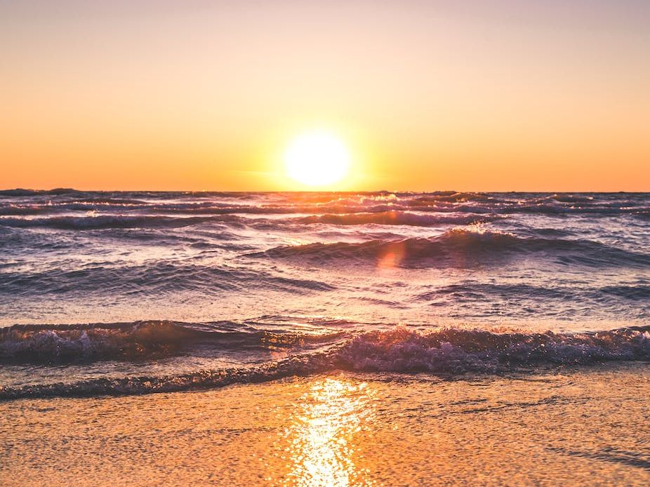 The sun is setting over the ocean and the waves are crashing on the beach.