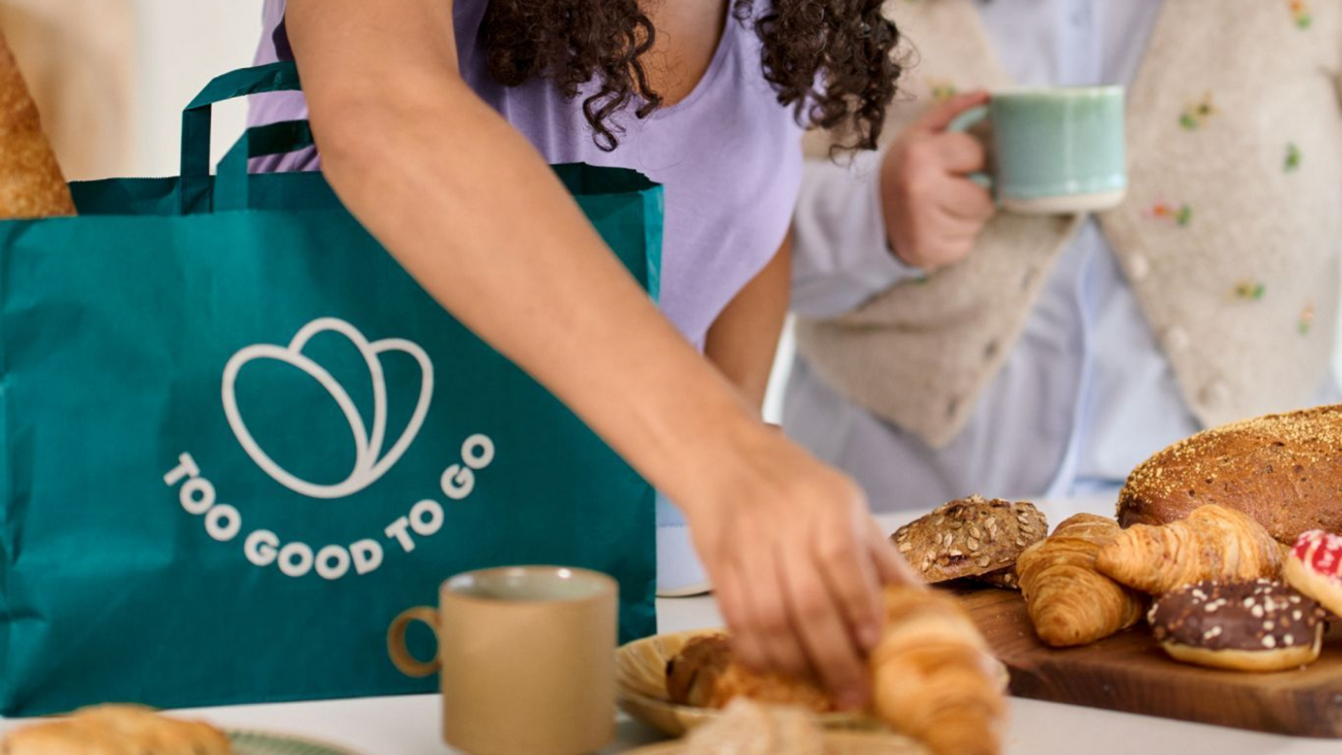 People gathering around a table with baked goods and a Too Good To Go bag.