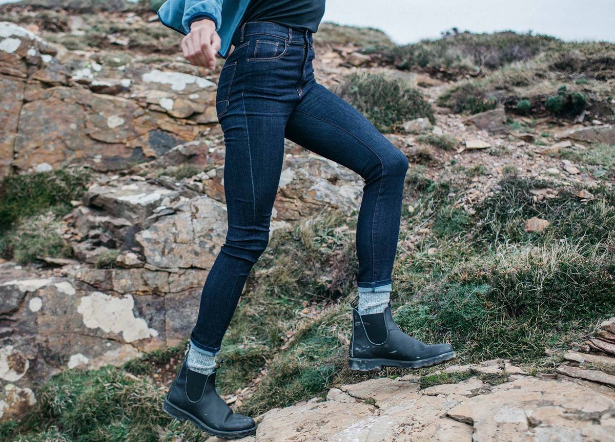 A woman is walking up a rocky hill wearing skinny jeans and black boots.