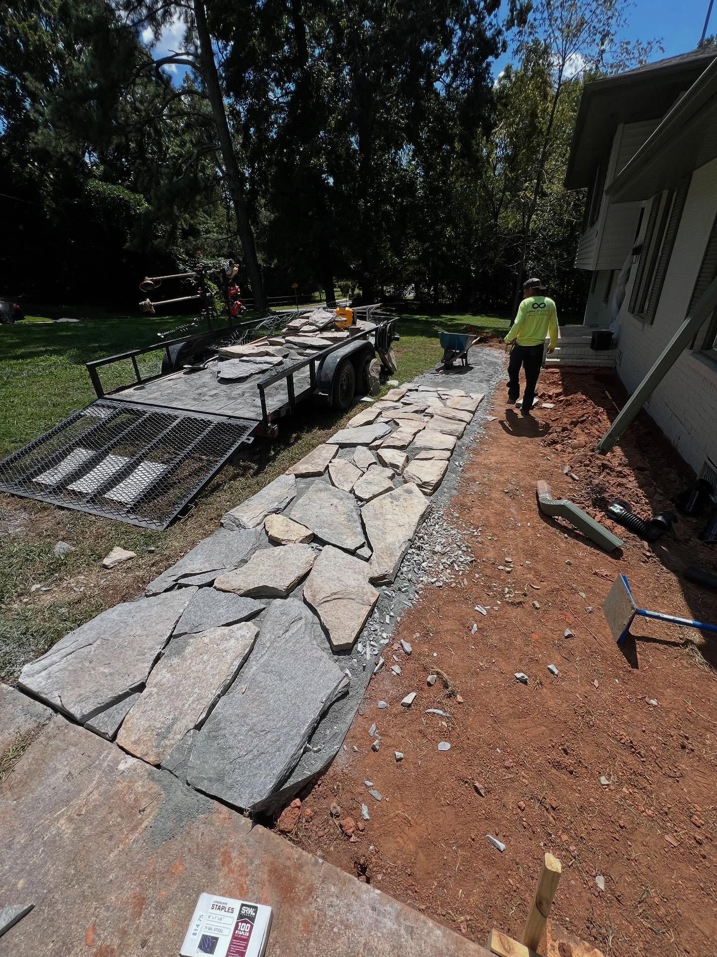 Workers laying a flagstone walkway beside a house, with one worker in a neon shirt and gravel edging