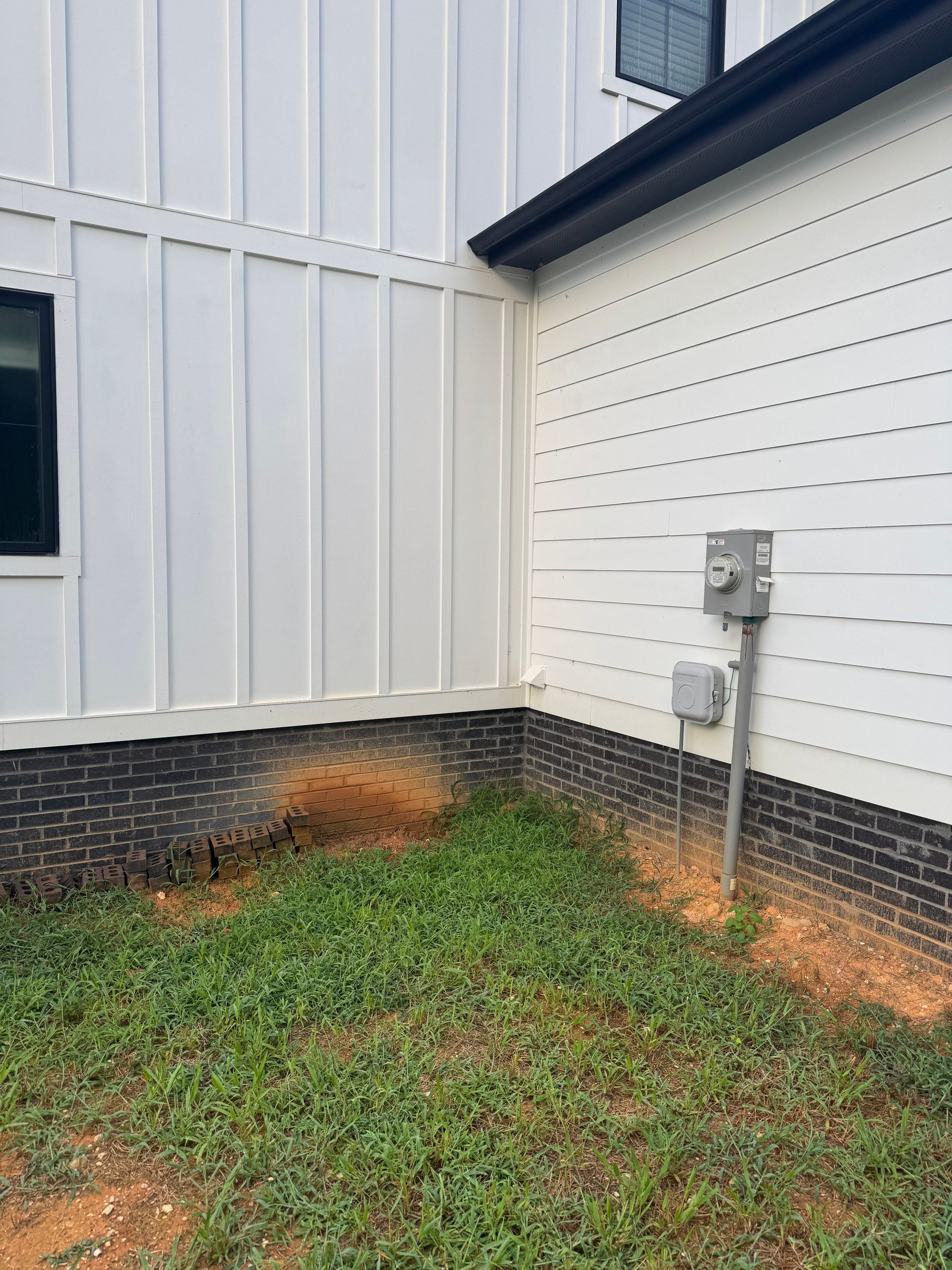 Exterior corner of a white house with green grass, brick foundation, and utility meters on the wall