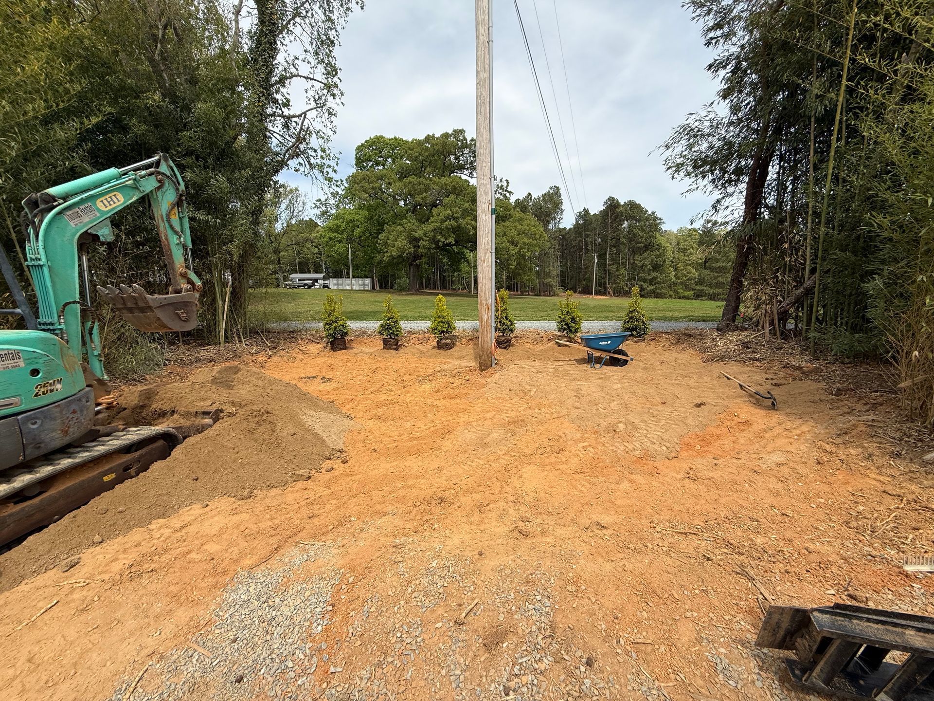 Construction site with excavator, gravel spread, and utility pole in a wooded area