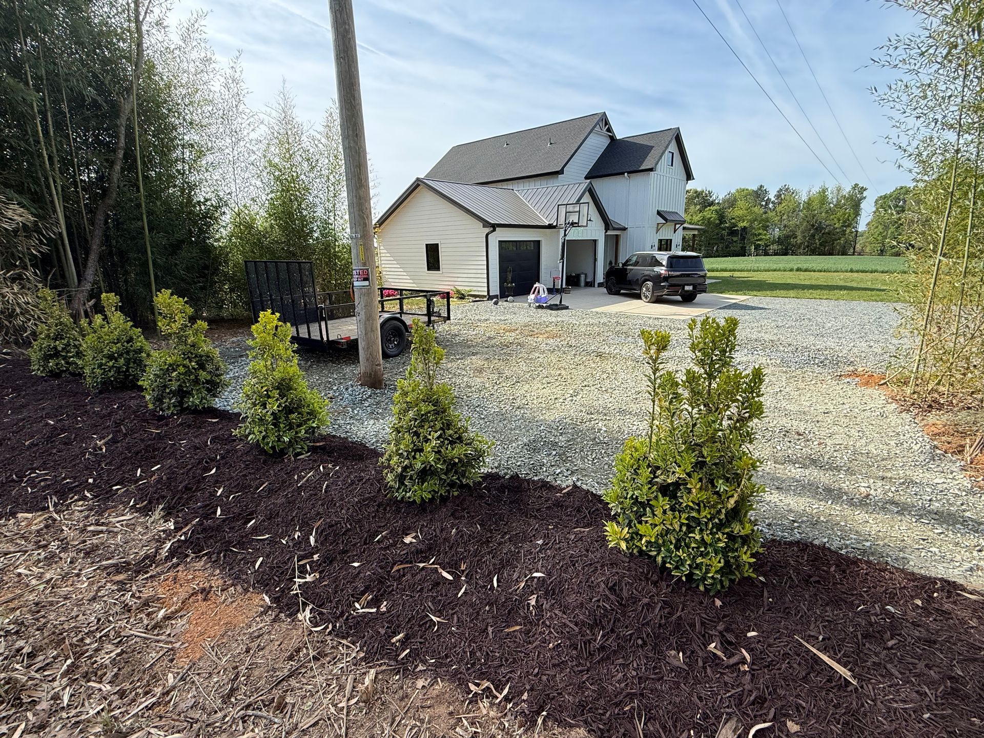 Gravel driveway leading to a white house with dark roof, newly mulched flower bed, and a parked SUV.