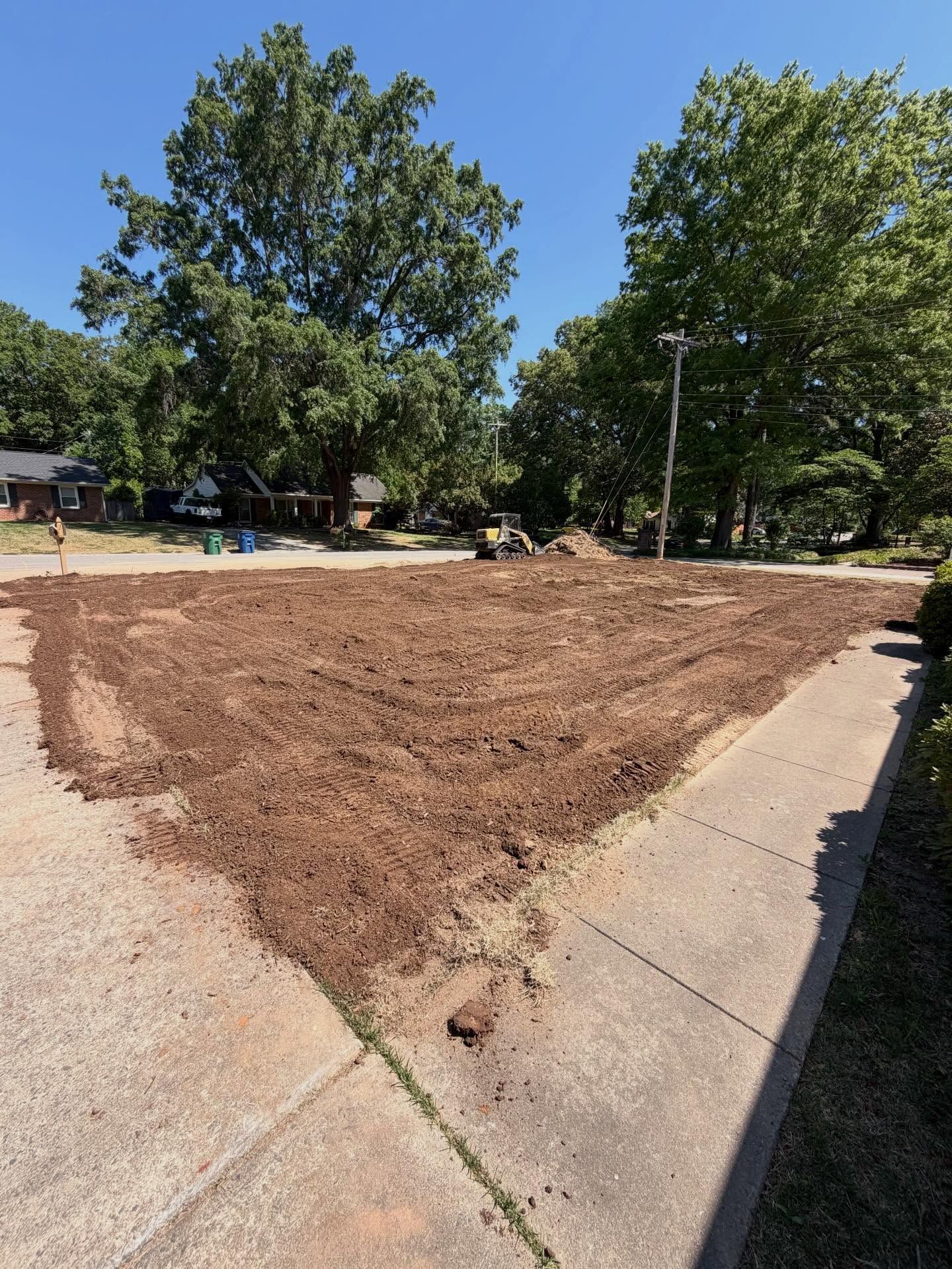 Fresh brown mulch spread over a curved concrete path in a park, with trees and blue sky nearby