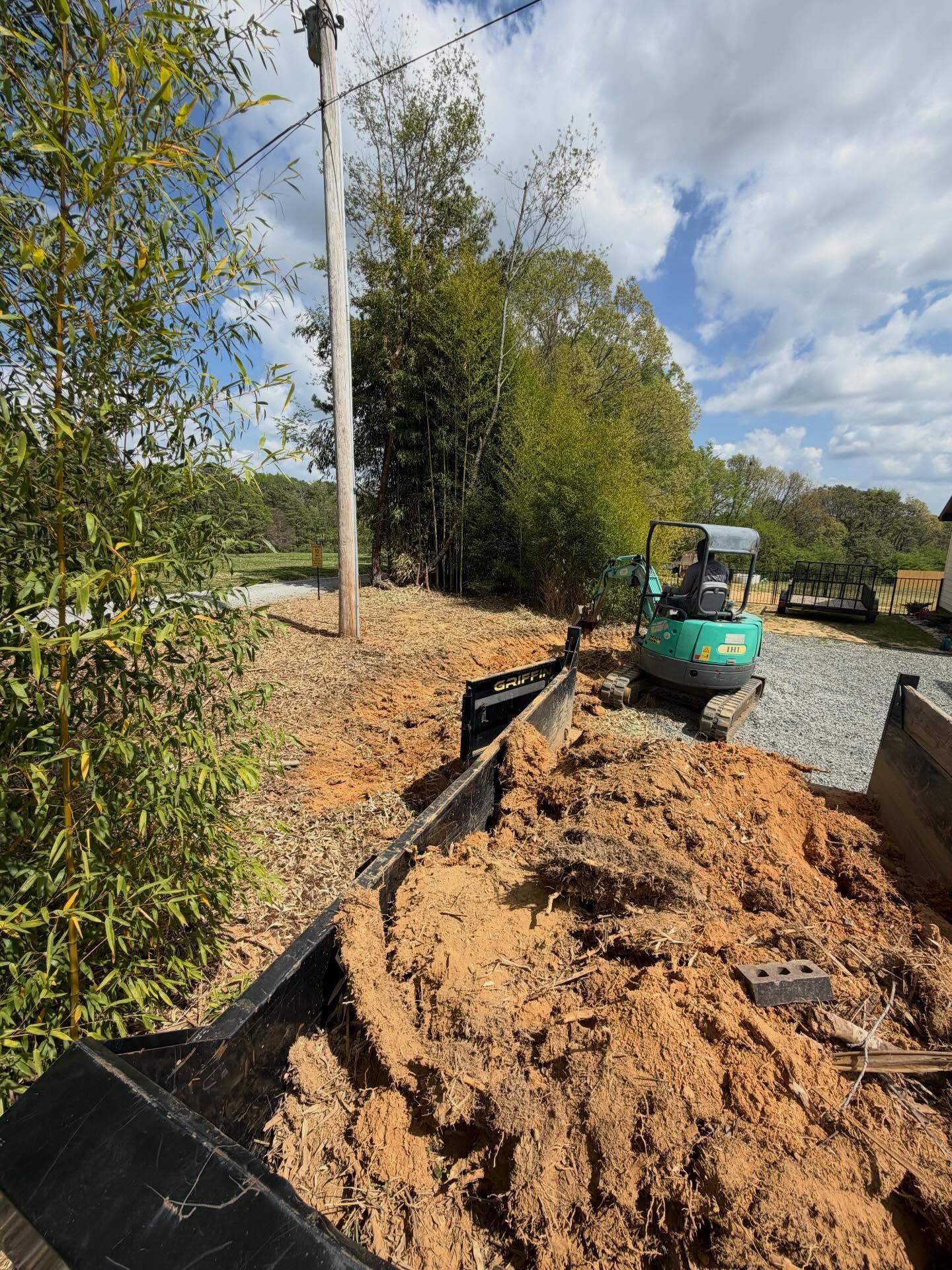 Mini excavator digging a trench beside a gravel path and utility pole on a cloudy day