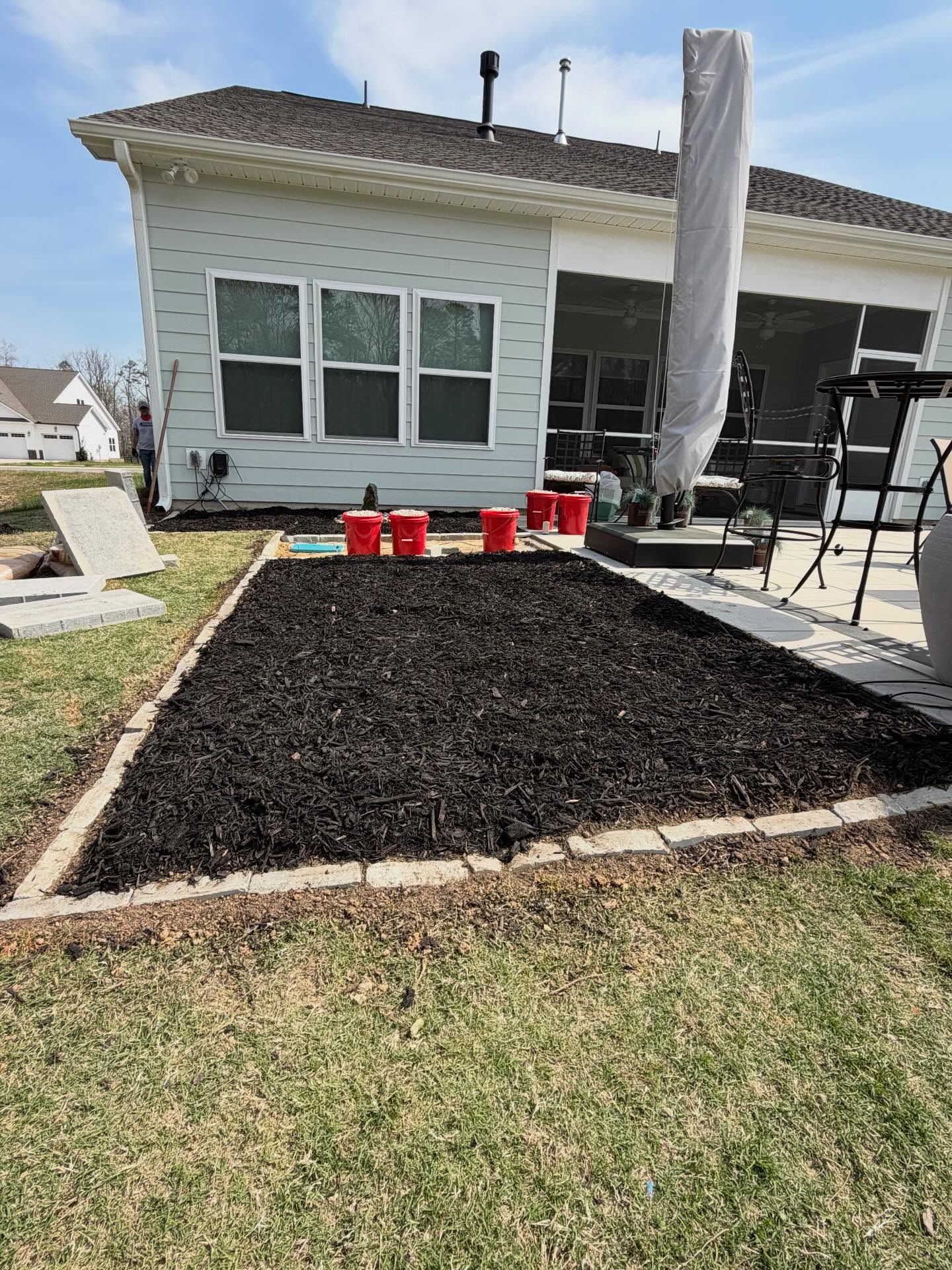 Backyard patio with black mulch bed, white house, and patio furniture under a covered section