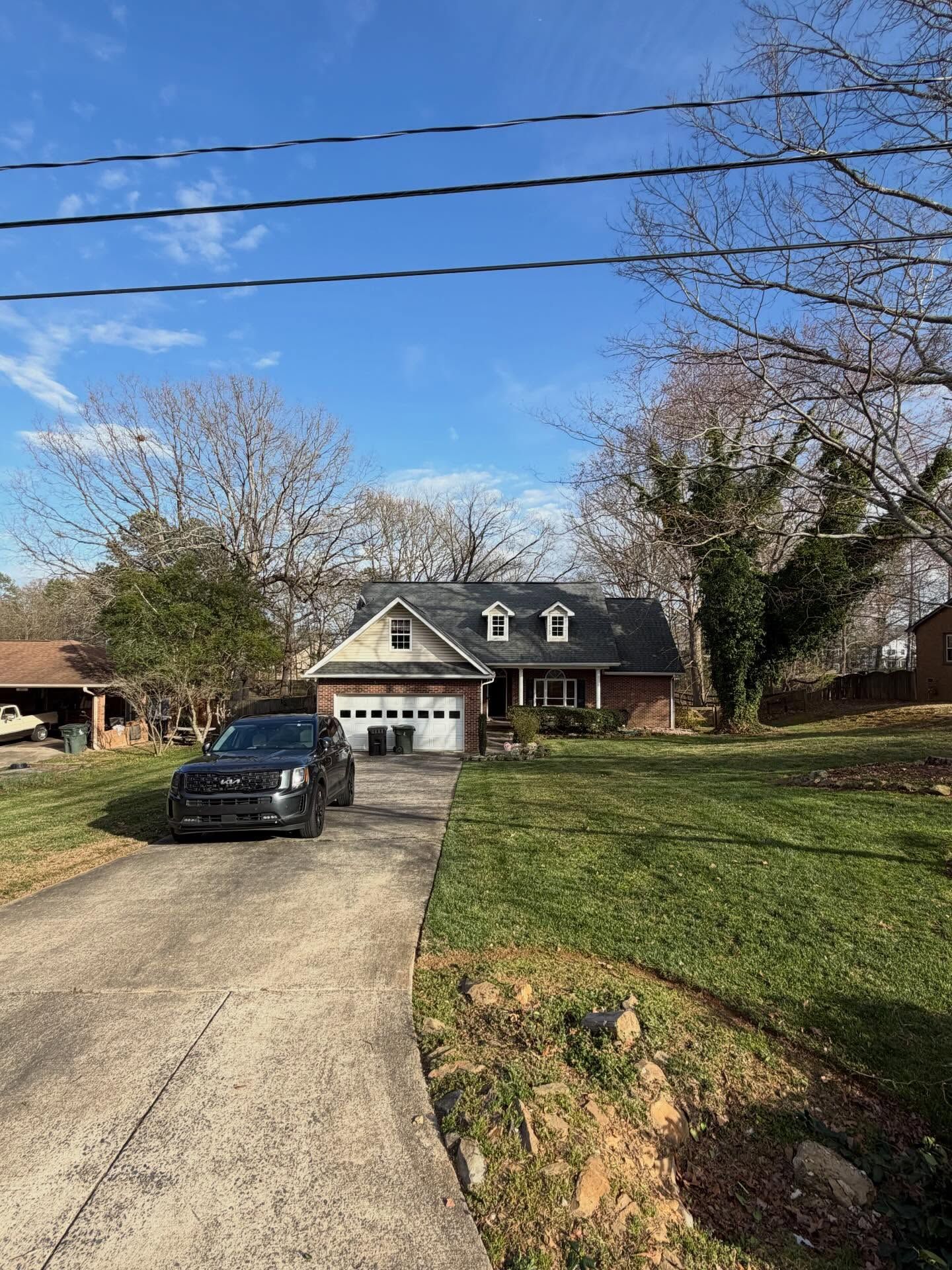 Suburban house with a black car in the driveway, leafless trees, and a blue sky overhead