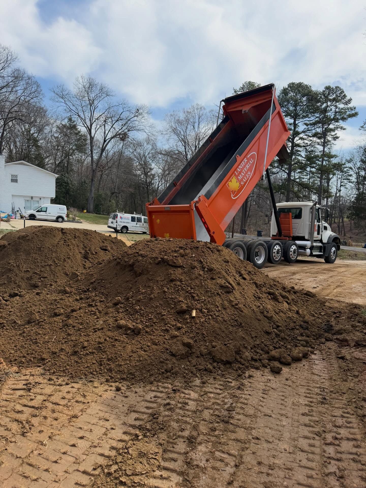 Orange dump truck unloading dirt onto a large pile at a construction site