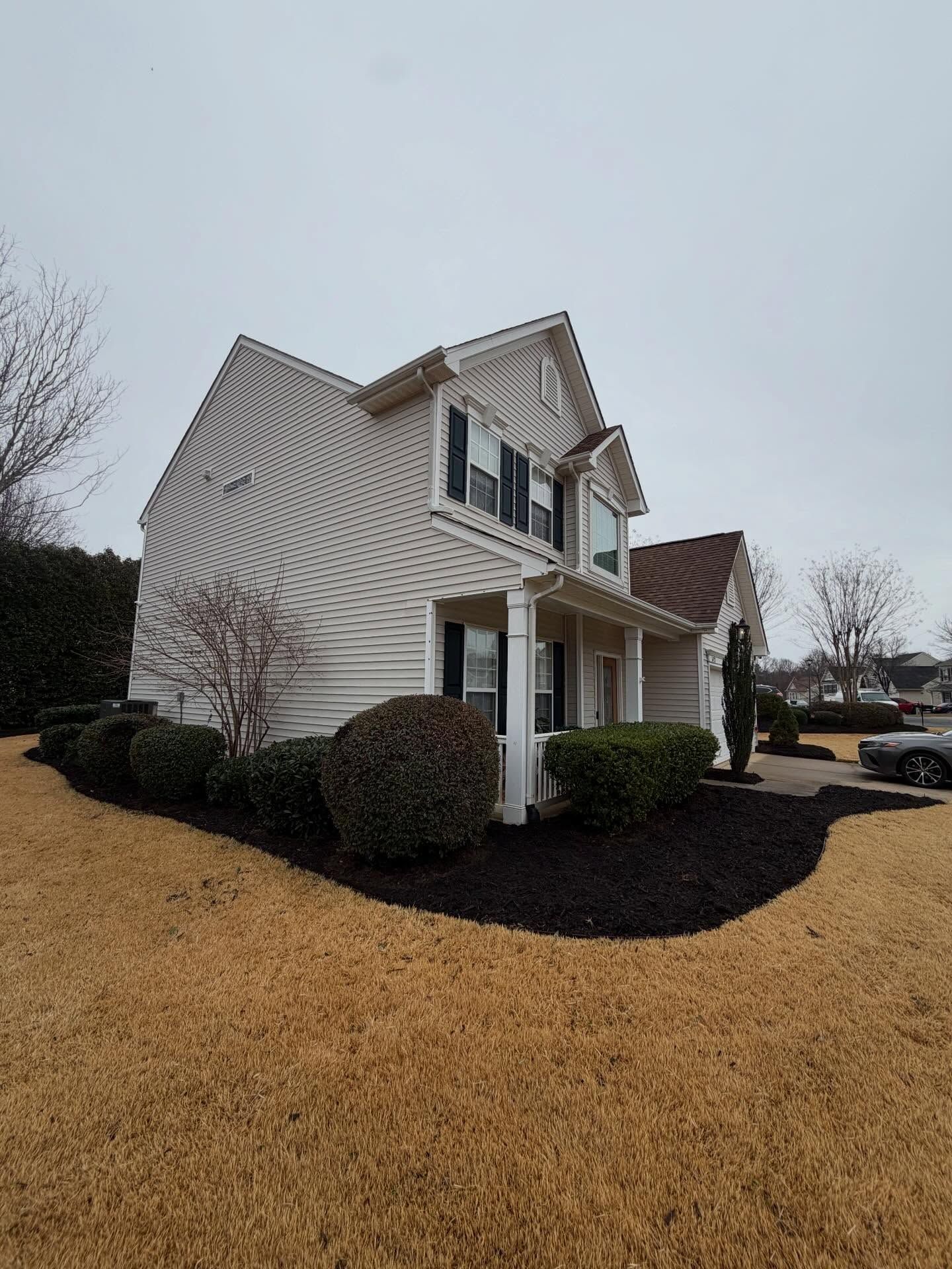 Suburban two-story house with white siding, dark shutters, brown roof, and winter lawn under overcast sky