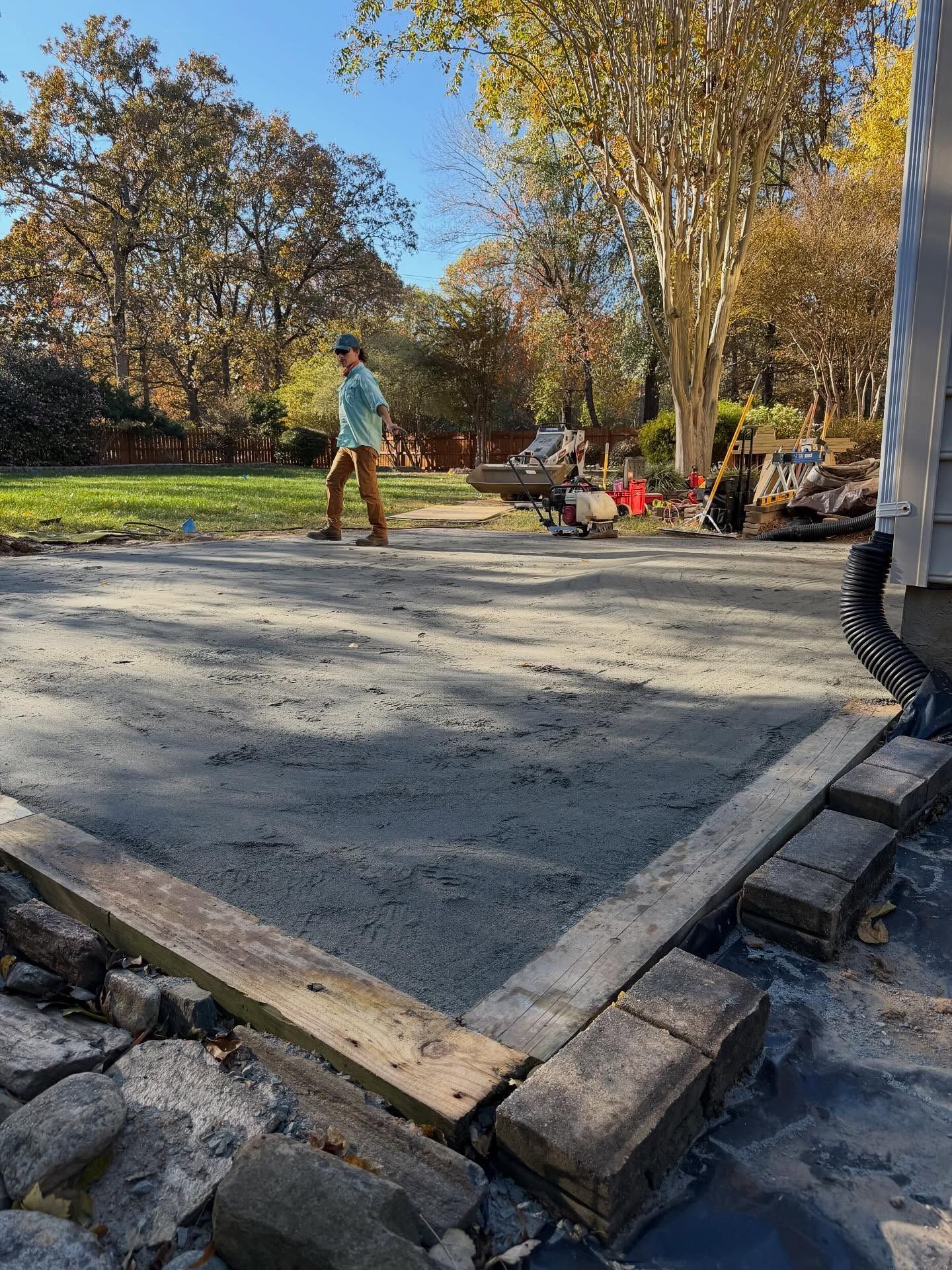 Fresh concrete slab beside a roadside, with a worker in a teal shirt and trees in the background