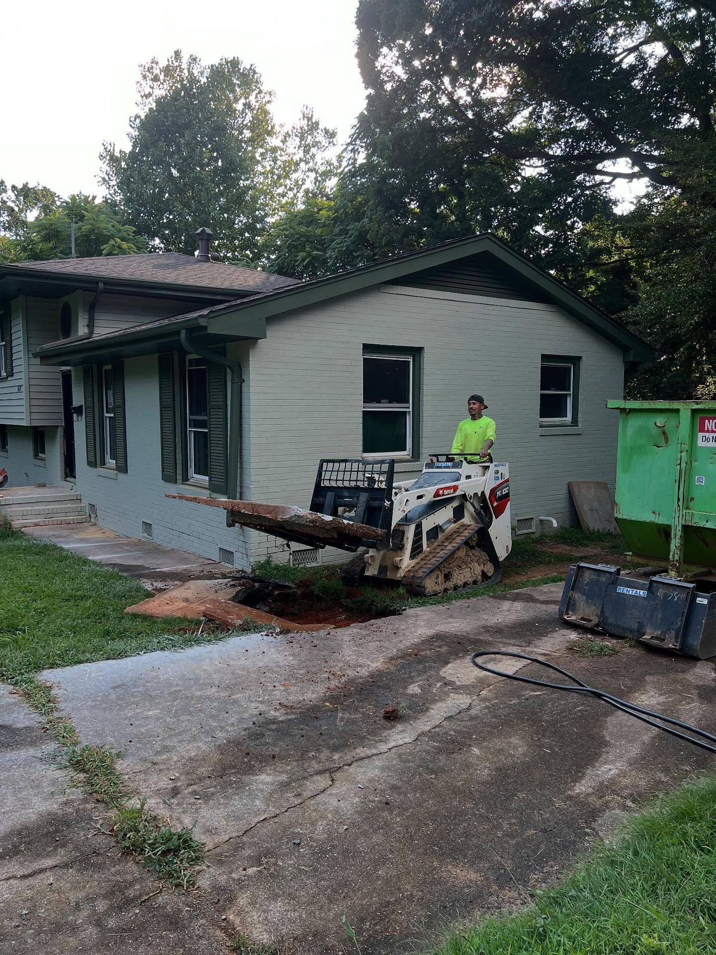 Small house with storm damage, debris in driveway, and a worker standing near a dumpster.
