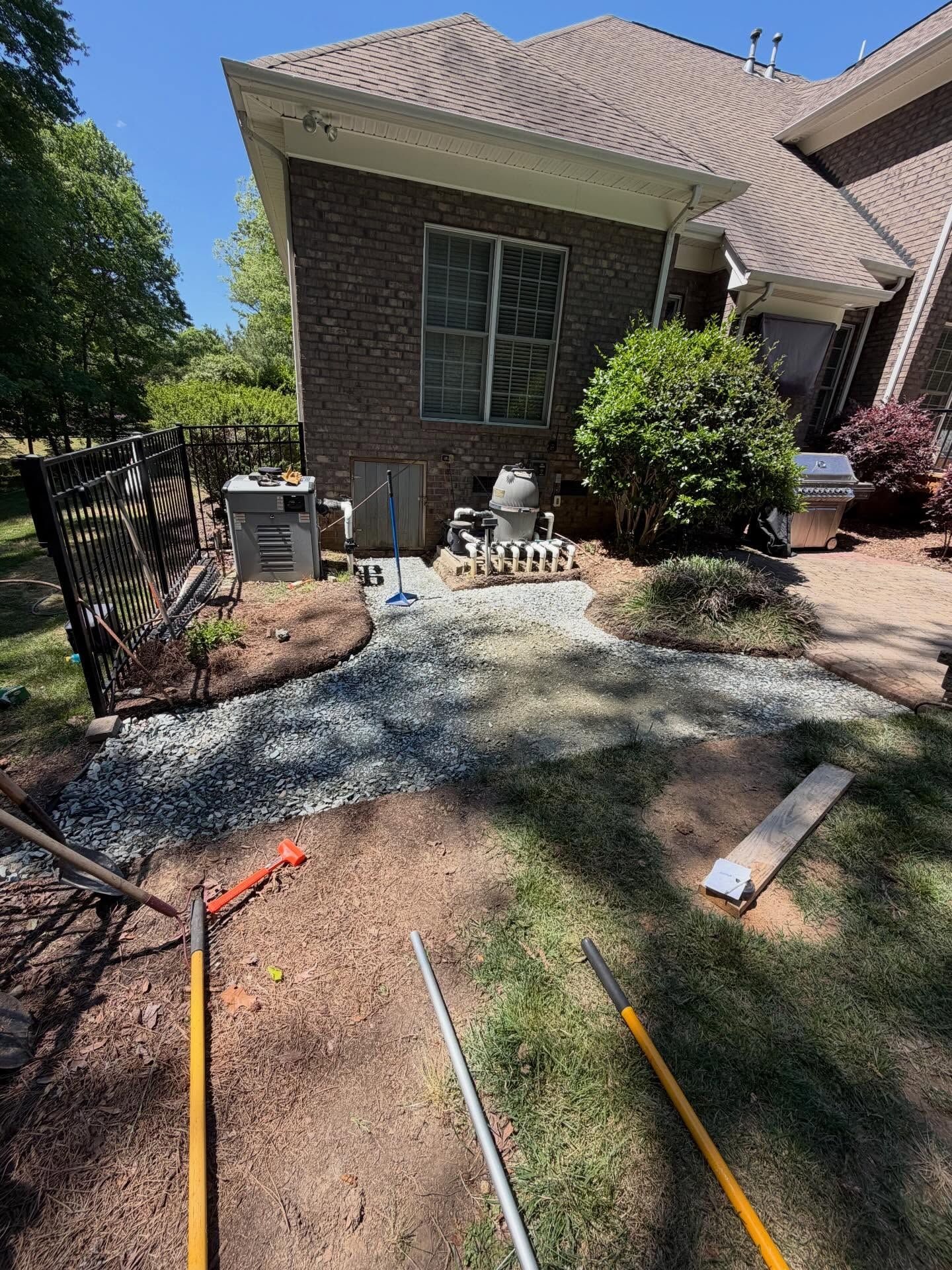 Backyard patio and house wall with gravel work area, tools, and newly laid border edging.