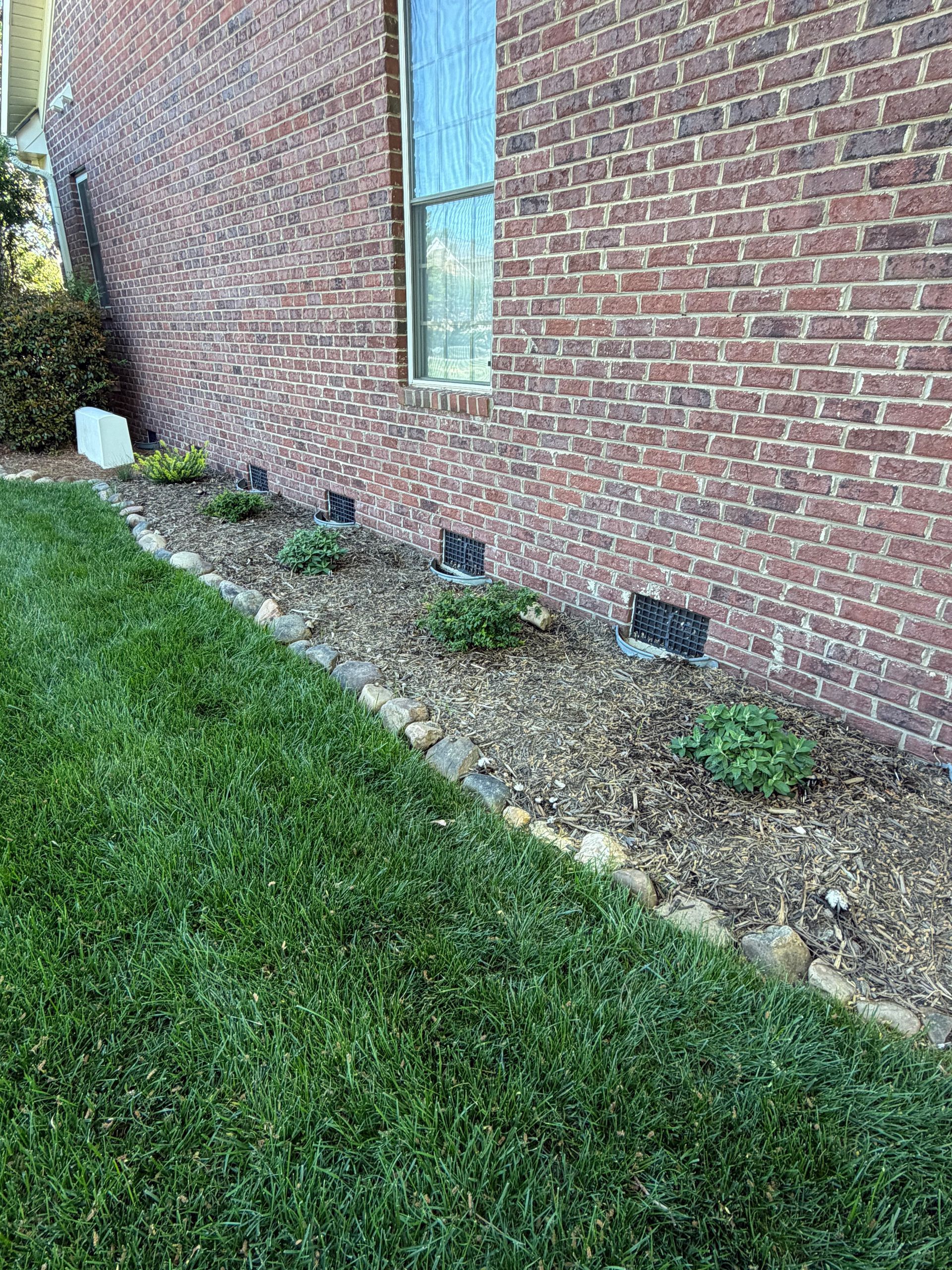 Brick house wall with a window and small flower bed beside a green lawn