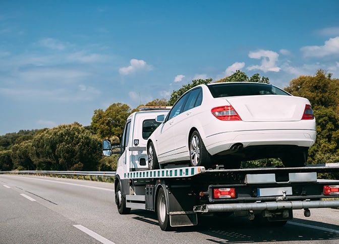 A White Car is Being Towed by a Tow Truck on a Highway — Mick’s Towing Service Pty Ltd in Carrara, QLD