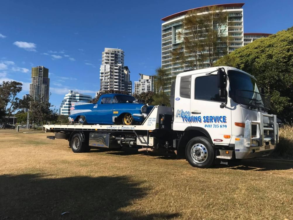 A Tow Truck with A Blue Car on The Back Is Parked in A Field — Mick's Towing Service Pty Ltd in Carrara, QLD