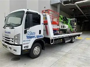 A White Towing Truck is Parked in a Parking Lot Next to a Building — Mick's Towing Service Pty Ltd in Carrara, QLD