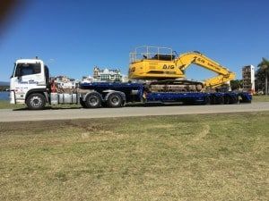 A Truck is Carrying a Large Yellow Excavator on a Trailer — Mick’s Towing Service Pty Ltd in Carrara, QLD