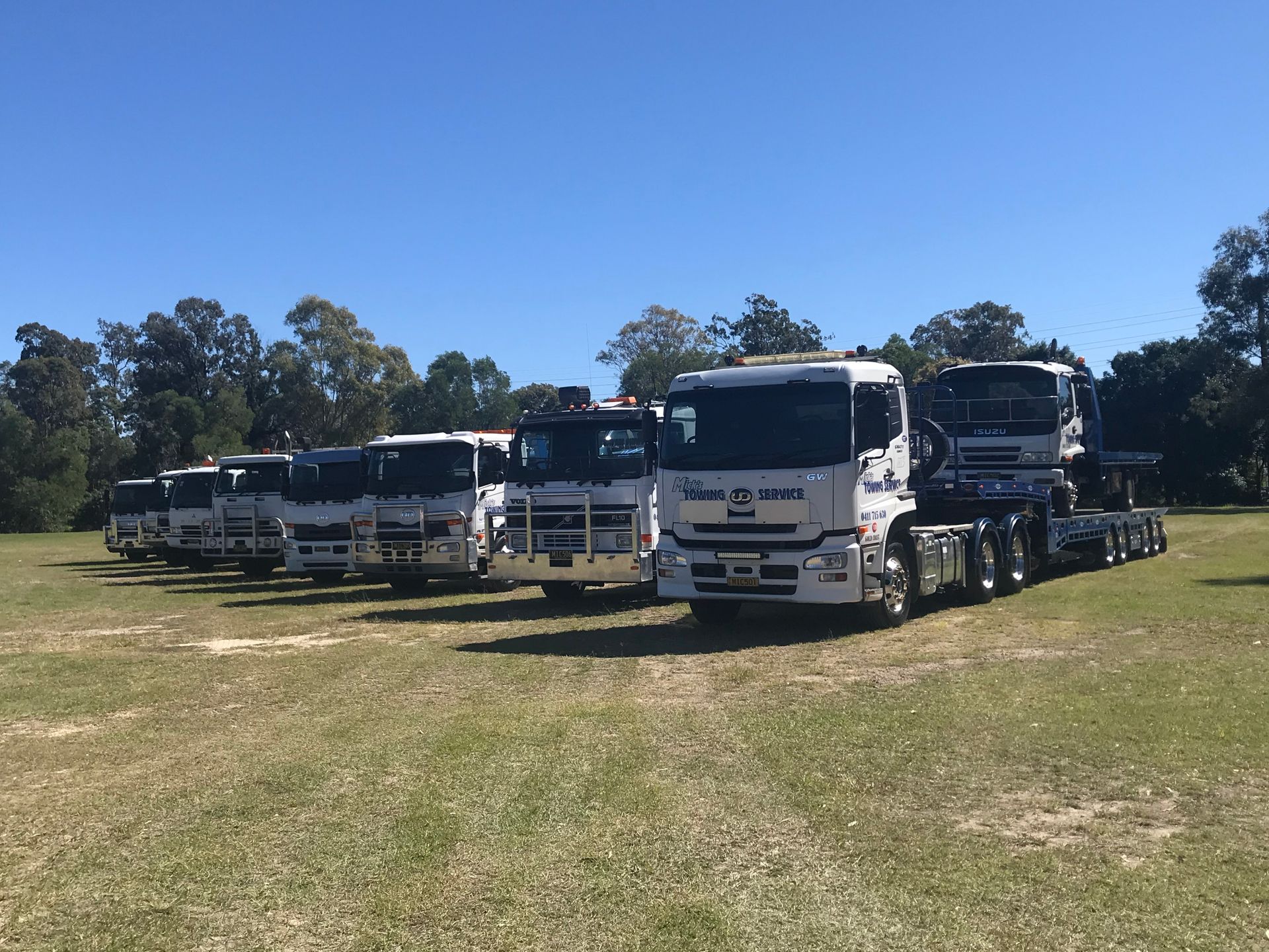 A Row of Tow Trucks Are Parked on a Grassy Field — Mick's Towing Service in Carrara, QLD