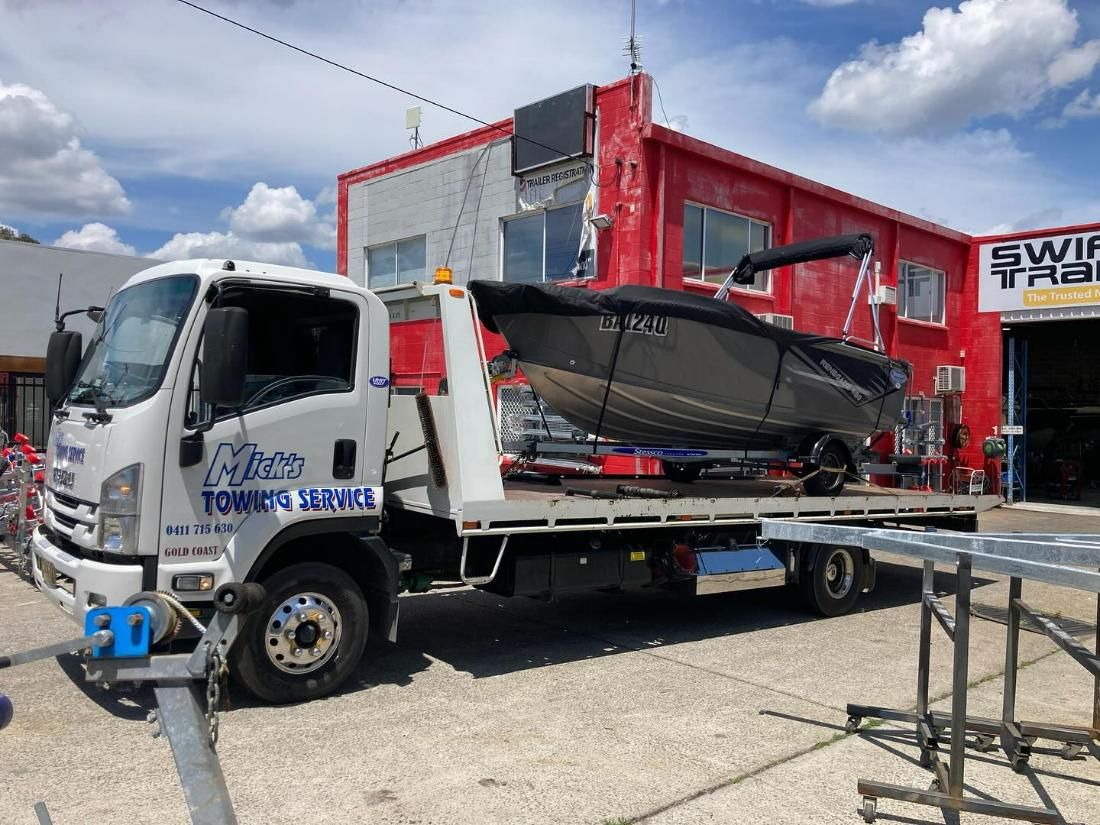 A Tow Truck Is Carrying a Boat on The Back of It — Mick's Towing Service Pty Ltd in Carrara, QLD