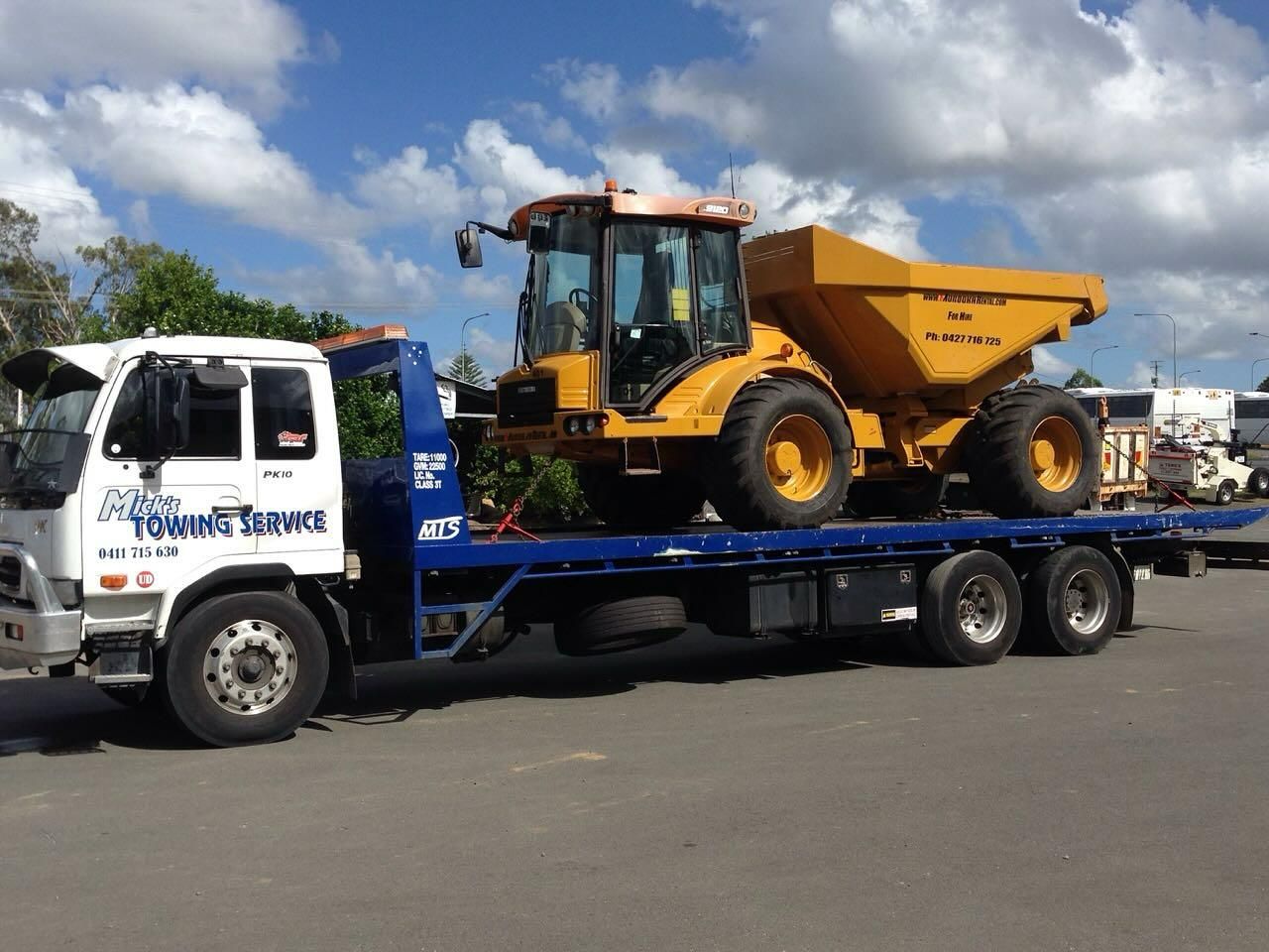 A Yellow Dump Truck Is Being Towed by A Towing Truck — Mick's Towing Service Pty Ltd in Carrara, QLD
