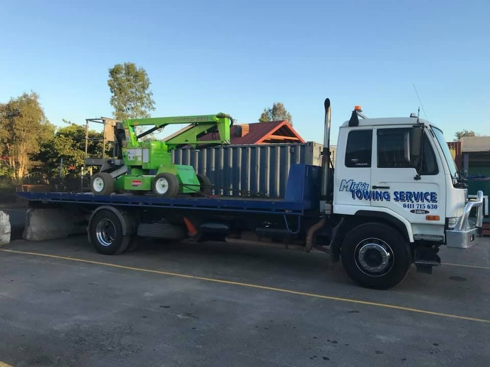 A Towing Truck With a Tractor on the Back is Parked on the Side of the Road — Mick's Towing Service Pty Ltd in Carrara, QLD