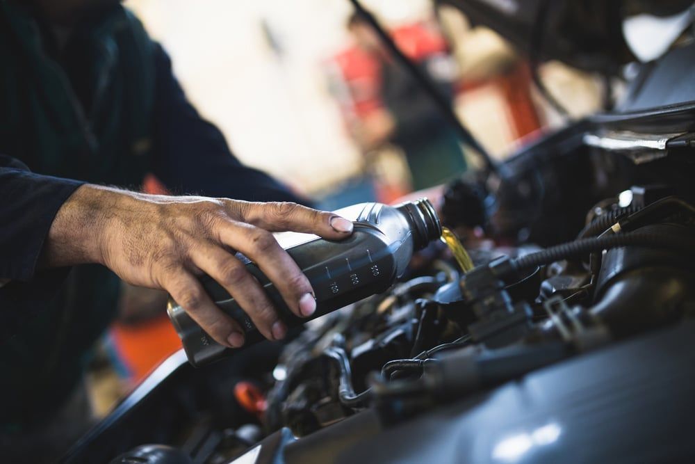 A Man is Pouring Oil Into a Car Engine — Mick’s Towing Service Pty Ltd in Carrara, QLD