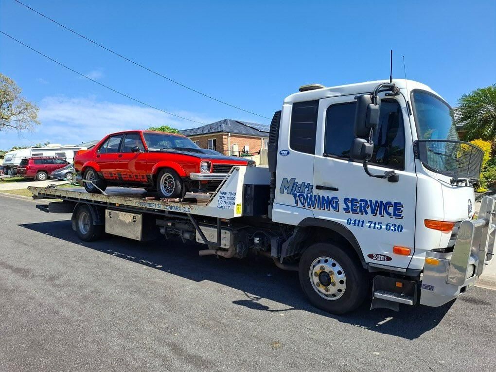 A Tow Truck with A Red Car on The Back Is Parked on The Side of The Road — Mick's Towing Service Pty Ltd in Carrara, QLD
