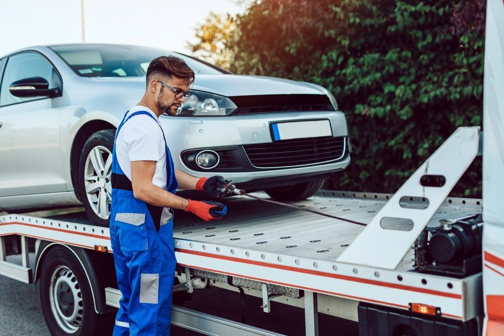 A Man is Standing Next to a Tow Truck With a Car on It — Mick’s Towing Service Pty Ltd in Carrara, QLD