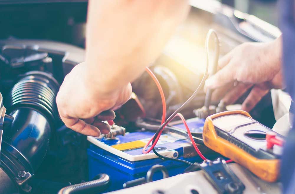 A Man is Working on a Car Battery With a Multimeter — Mick’s Towing Service Pty Ltd in Carrara, QLD