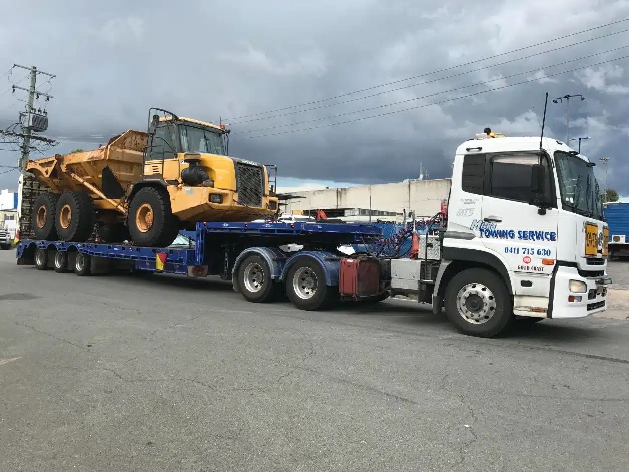 A Truck is Carrying a Large Yellow Bulldozer on a Trailer — Mick's Towing Service Pty Ltd in Carrara, QLD
