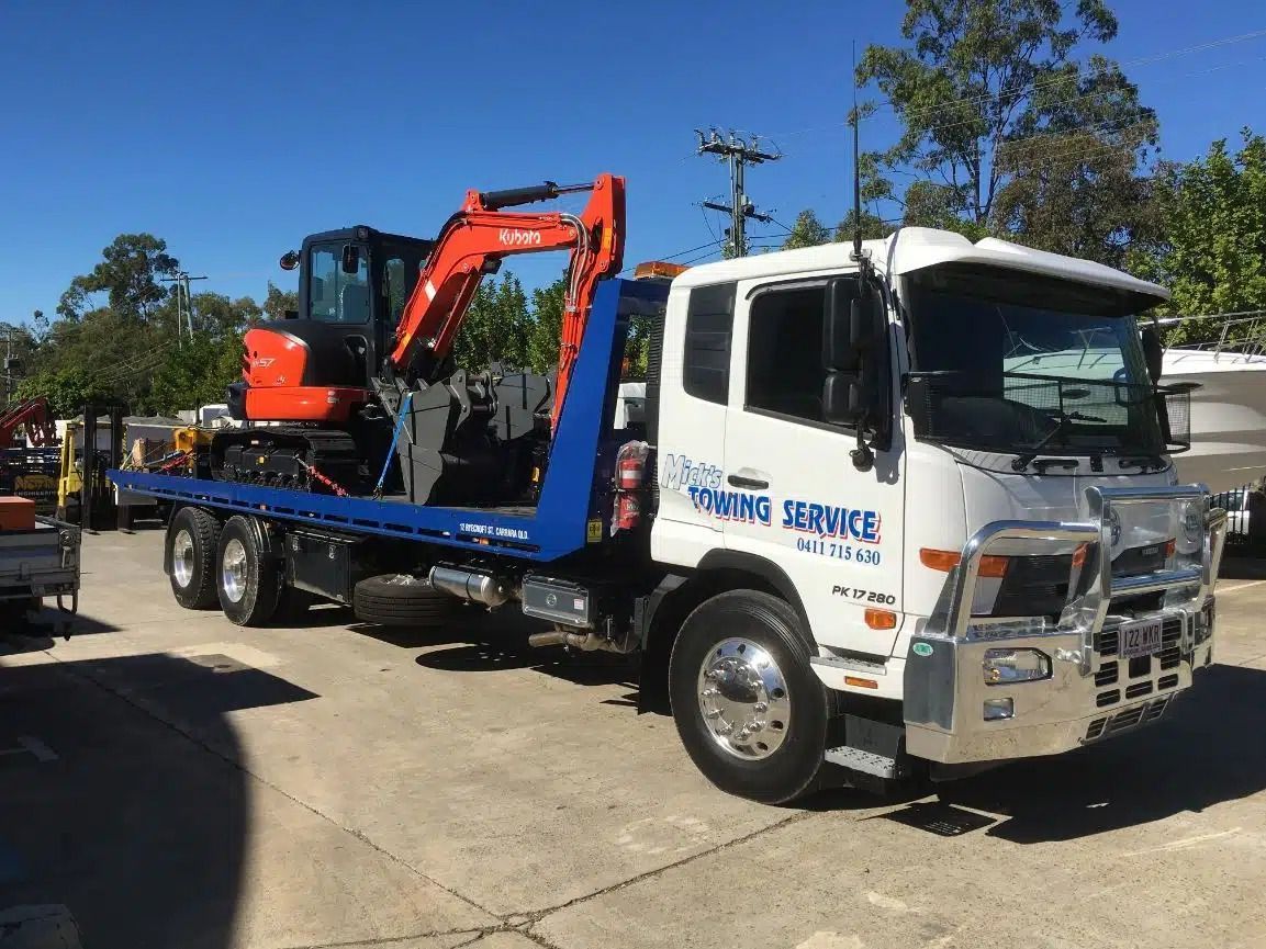 A Tow Truck With an Excavator on the Back is Parked in a Parking Lot — Mick's Towing Service Pty Ltd in Carrara, QLD