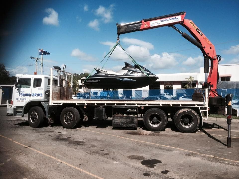 A Truck With a Crane Attached to It is Carrying a Jet Ski — Mick’s Towing Service Pty Ltd in Carrara, QLD