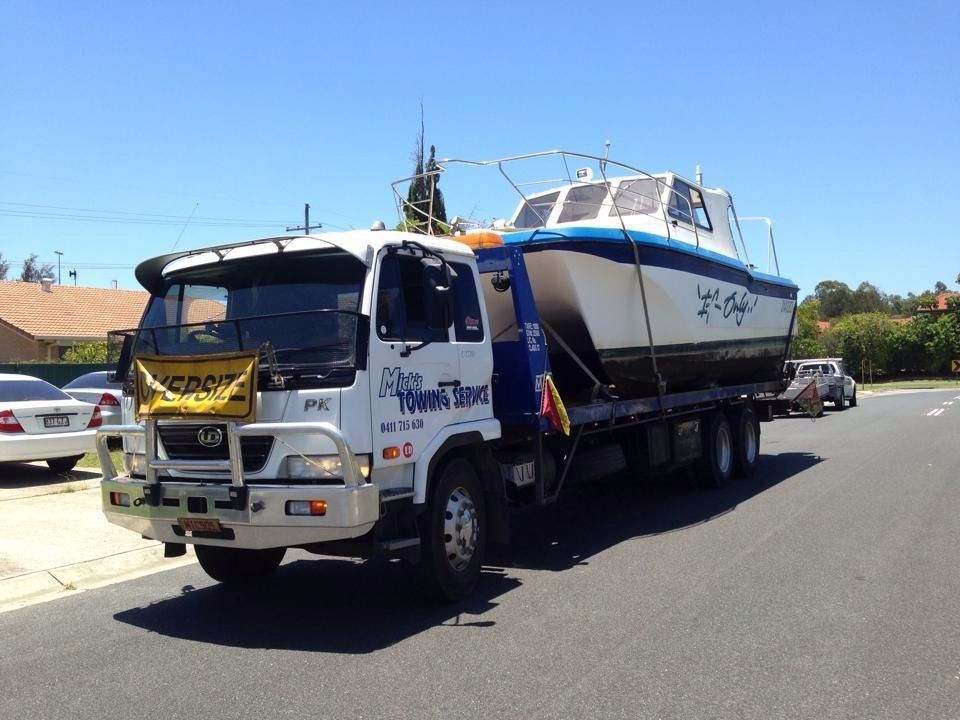 A Tow Truck is Carrying a Boat Down the Road — Mick’s Towing Service Pty Ltd in Carrara, QLD