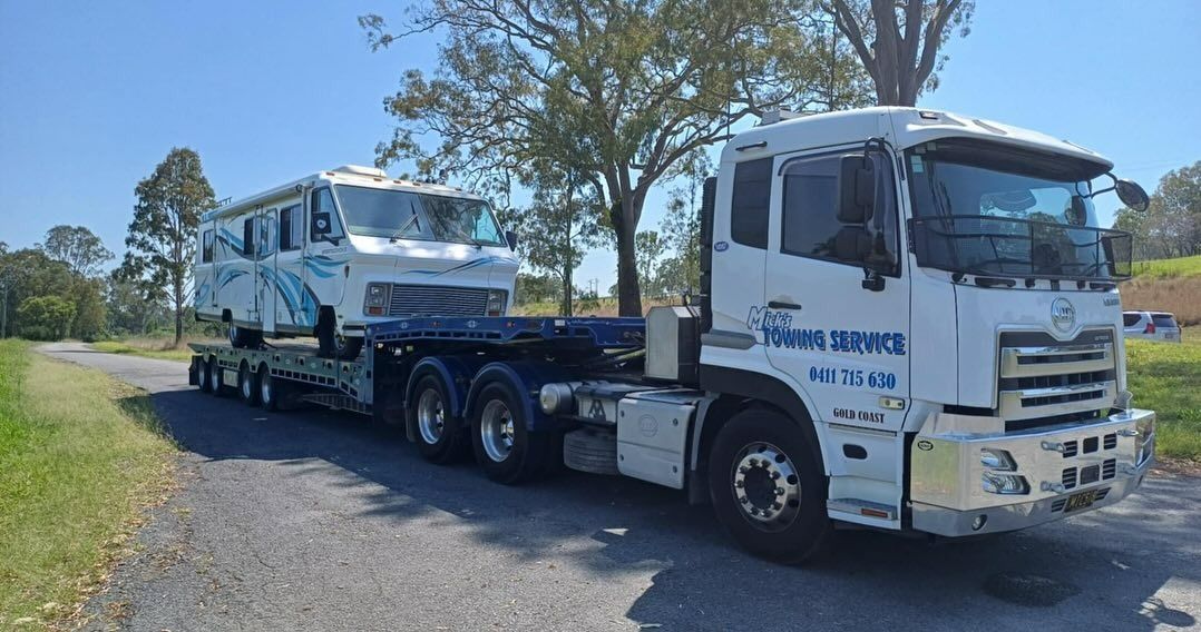 A Semi Truck is Driving Down a Road Next to a Tree — Mick's Towing Service in Carrara, QLD
