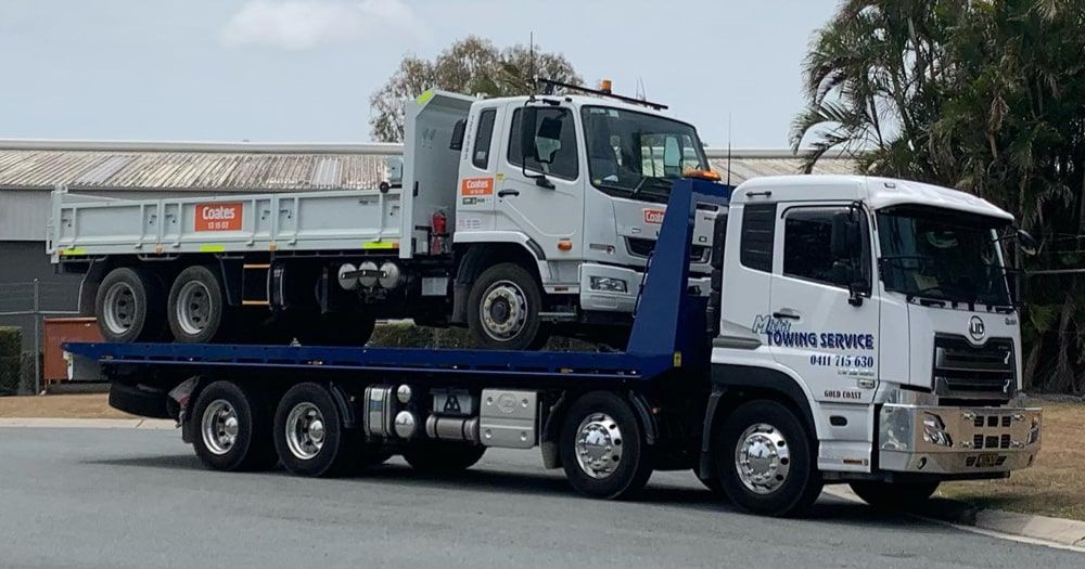 A Tow Truck is Carrying a Dump Truck on the Back of It — Mick's Towing Service in Carrara, QLD