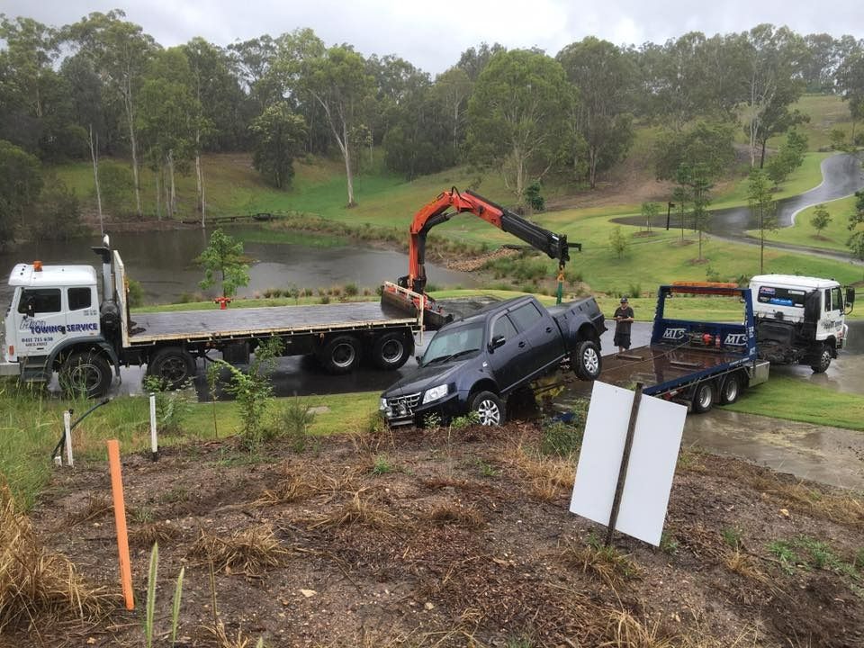 A Black Truck is Being Towed by a Flatbed Truck — Mick's Towing Service Pty Ltd in Carrara, QLD