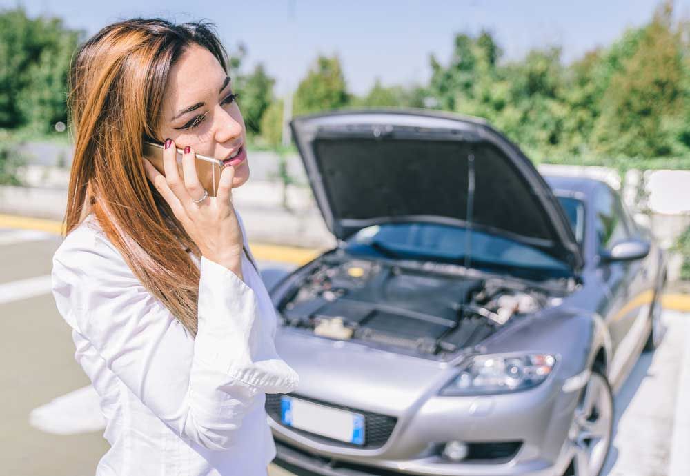 A Woman is on a Cell Phone in Front of a Broken Down Car — Mick’s Towing Service Pty Ltd in Carrara, QLD