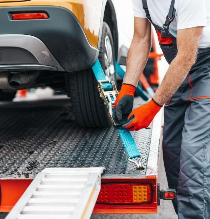 A Man is Tying a Car to a Tow Truck — Mick's Towing Service Pty Ltd in Carrara, QLD