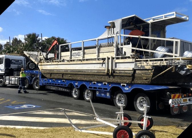 A Large Blue Truck is Carrying a Boat on a Trailer — Mick's Towing Service Pty Ltd in Carrara, QLD