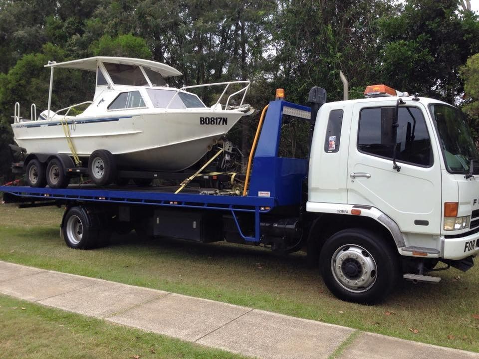 A Tow Truck is Carrying a Boat on the Back of It — Mick's Towing Service Pty Ltd in Carrara, QLD