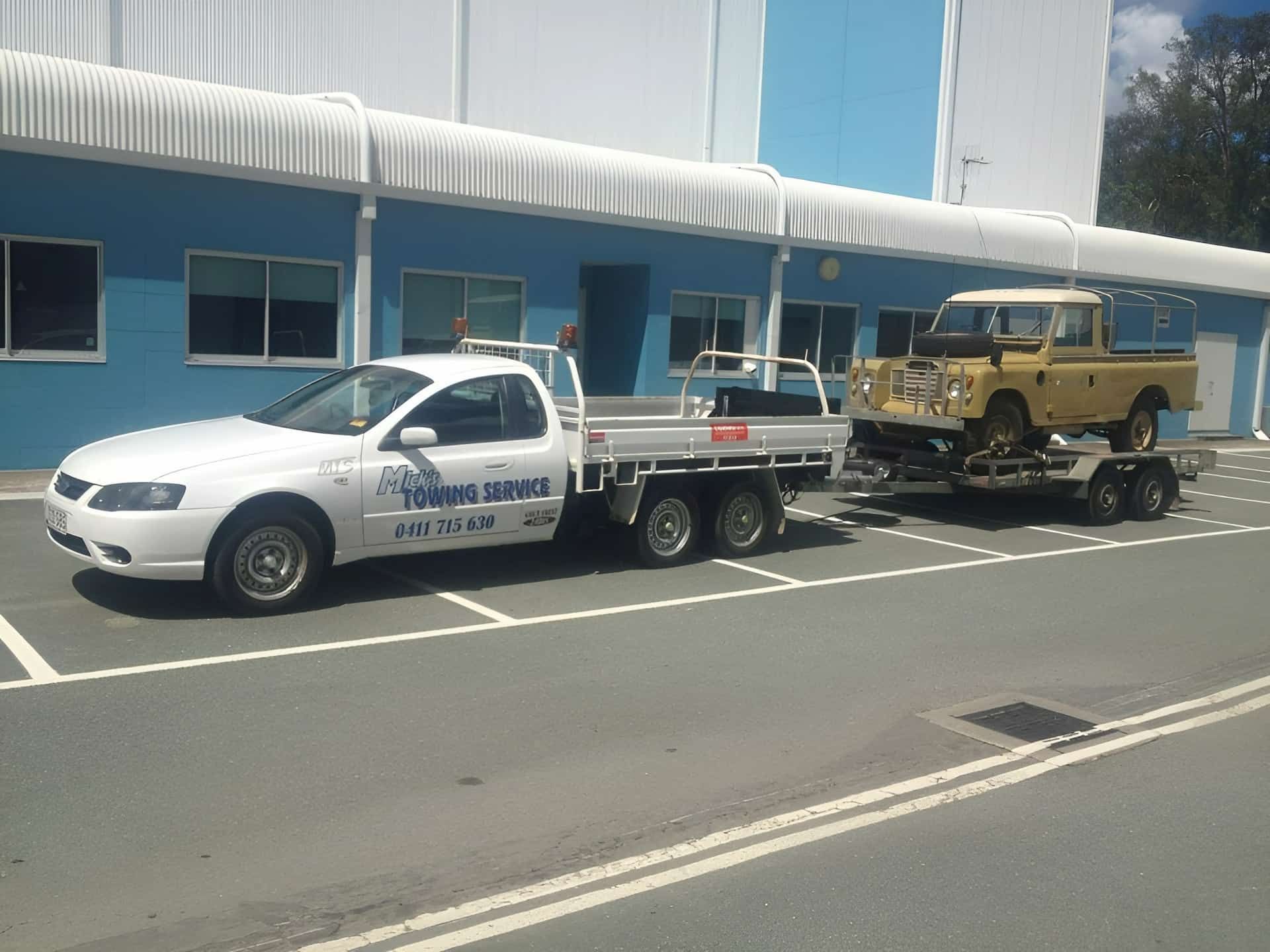 A White Truck is Towing a Yellow Land Rover on a Trailer — Mick's Towing Service Pty Ltd in Carrara, QLD