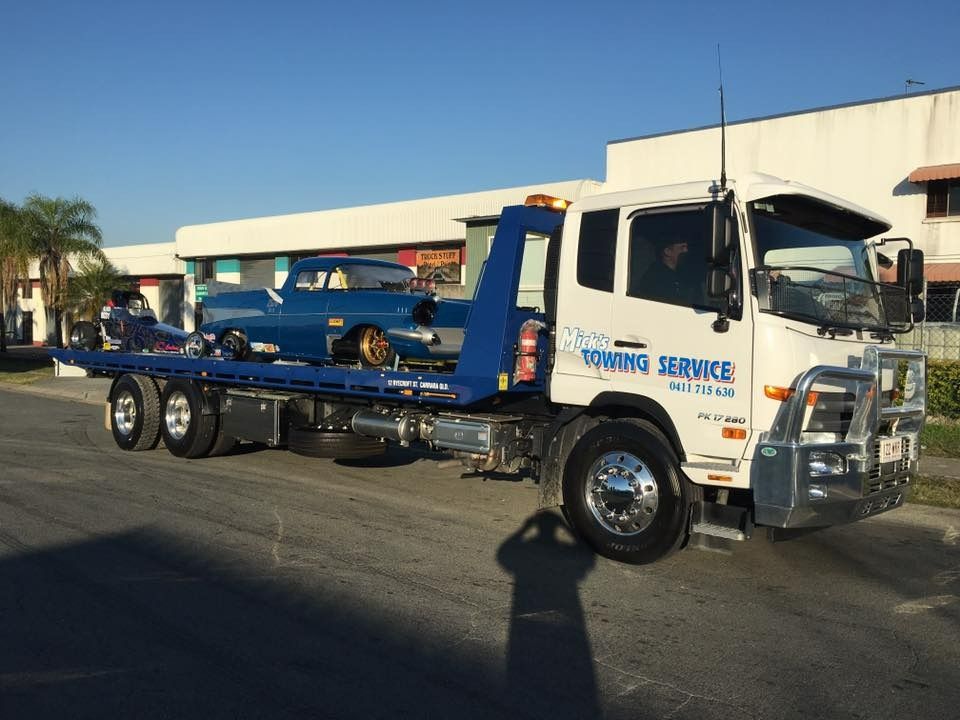A Tow Truck With a Car on the Back is Parked on the Side of the Road — Mick's Towing Service Pty Ltd in Carrara, QLD